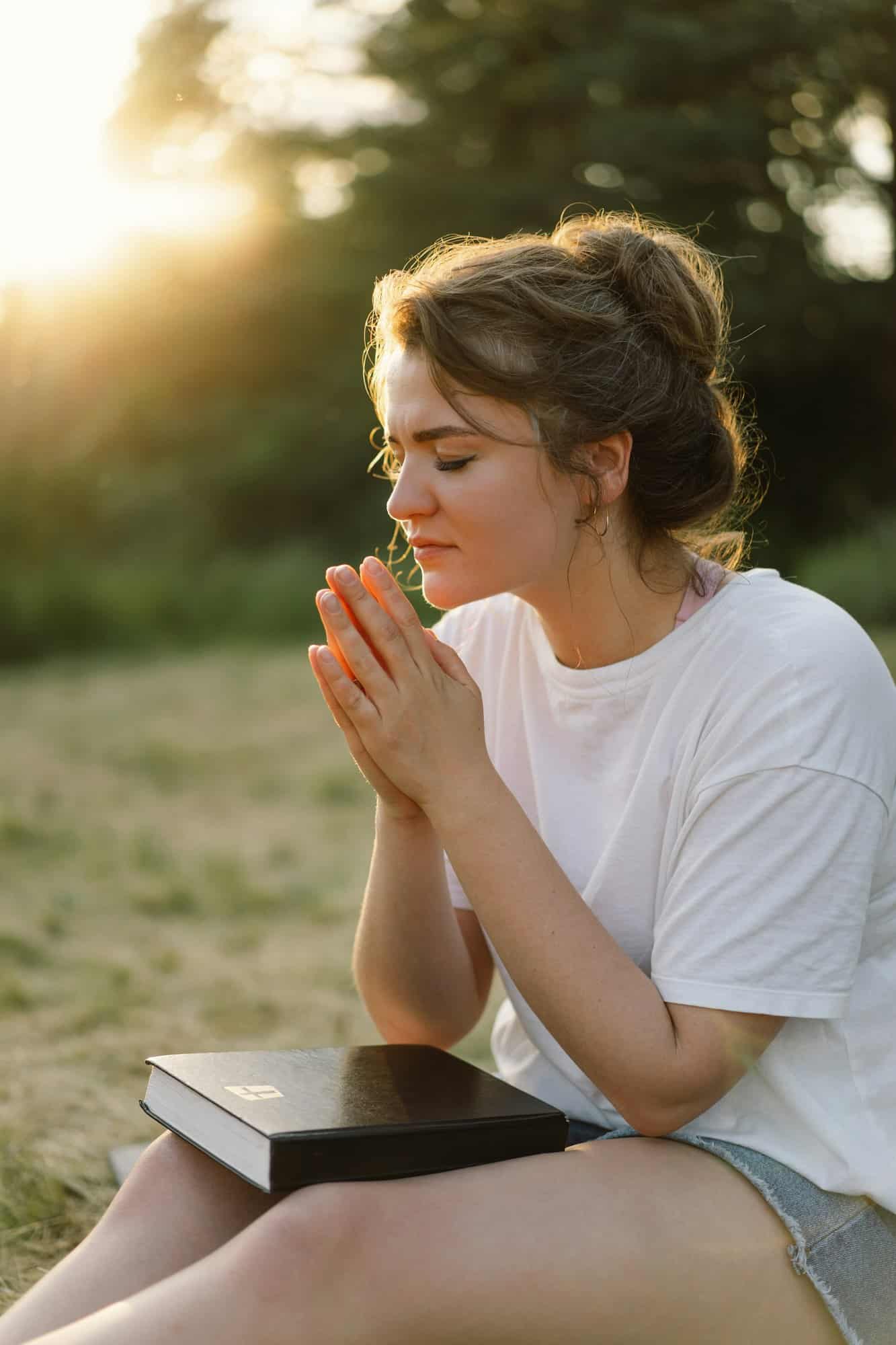 Woman closed her eyes, praying in a field during beautiful sunset.